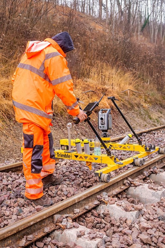 Construction worker with measuring device device works on yellow equipment on rails in winter, tamping machine on Hermann, Hesse, Bahn, Althengstett, Calw district, Germany