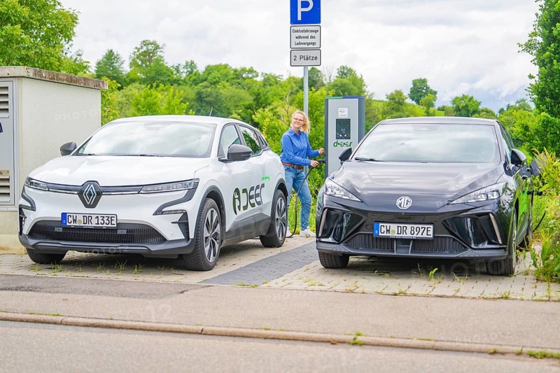 Two electric cars are parked at the outdoor charging station with a woman nearby, Deer E- Carsharing, Calw, Germany