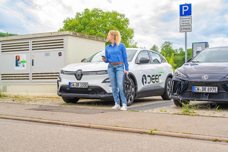 Woman in blue shirt standing between two electric cars in a parking lot, Deer E-Carsharing, Calw, Germany