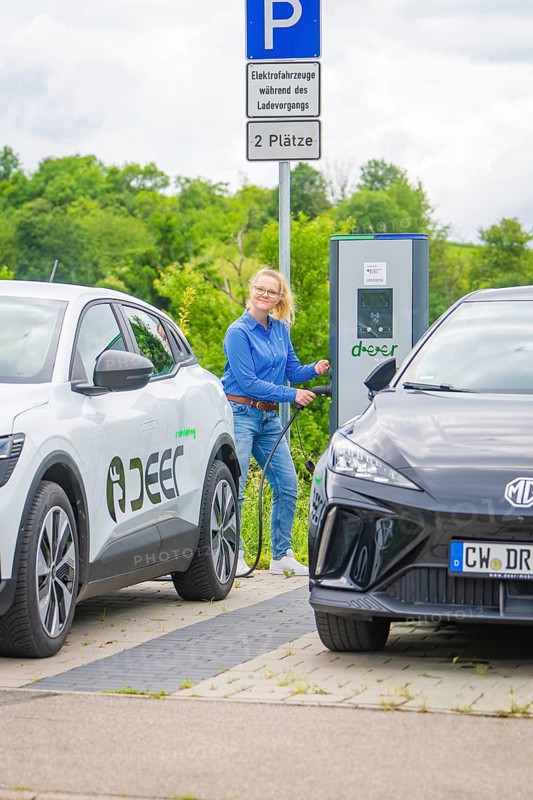 Woman refuels electric car at a charging station between two parked vehicles, Deer E-Carsharing, Calw, Germany