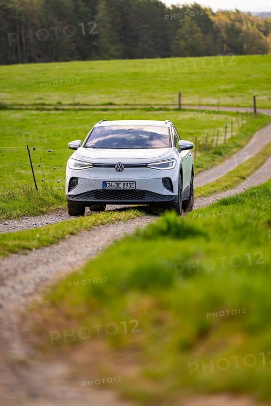 White car driving on a dirt road through green meadow landscape in daylight, Deer E-Carsharing, VW ID4, Calw, Germany