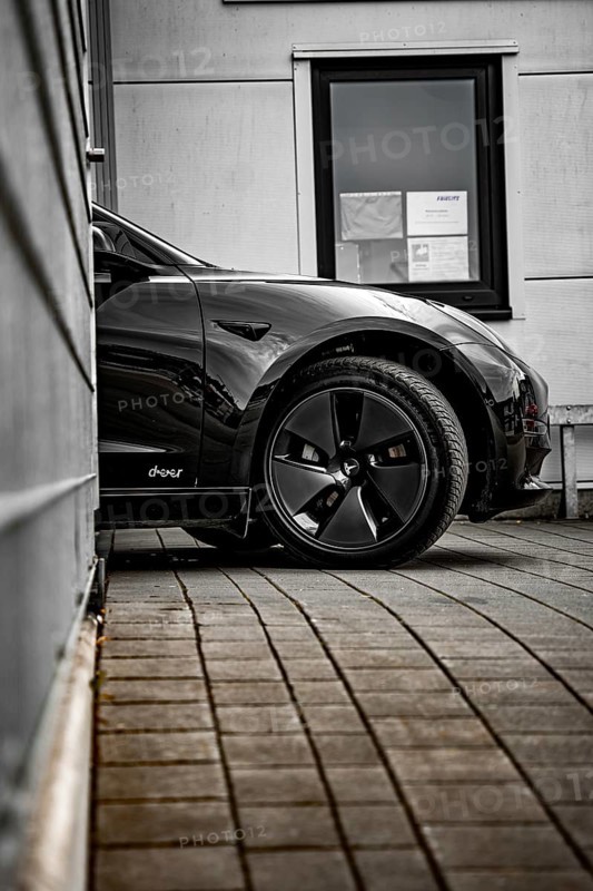Black car in front of a modern building with tiled floor and a window, Deer E-Carsharing, Tesla Model 3, Calw, Germany