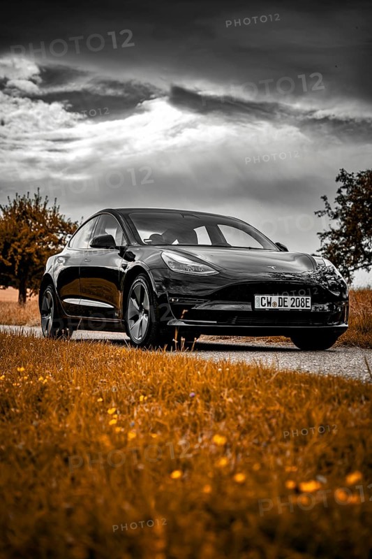 Black car on country road with orange fields under dramatic sky, Deer E- car sharing, Tesla Model 3, Calw, Germany