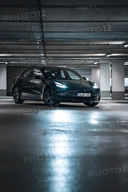 Black car in a modernly lit parking garage at night with reflective floor surfaces, Deer e-car sharing, Tesla Model 3, Calw, Germany