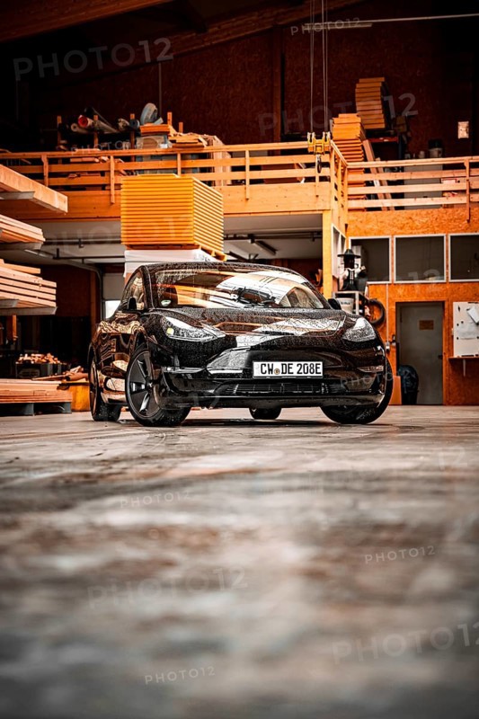 Black car in an industrial-looking workshop with wooden details, parked on concrete floor, deer e-car sharing, Tesla Model 3, Calw, Germany