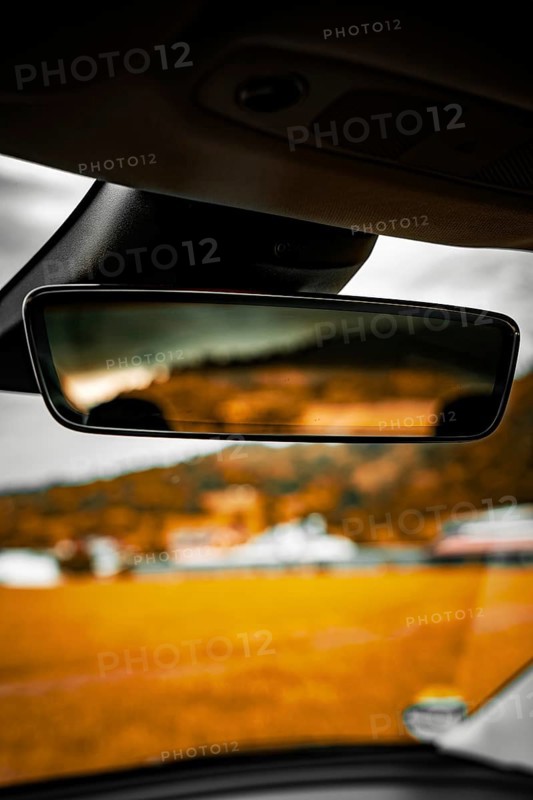 Rearview mirror in car with blurred view of landscape and buildings in background, Deer E-Carsharing, Tesla Model 3, Calw, Germany