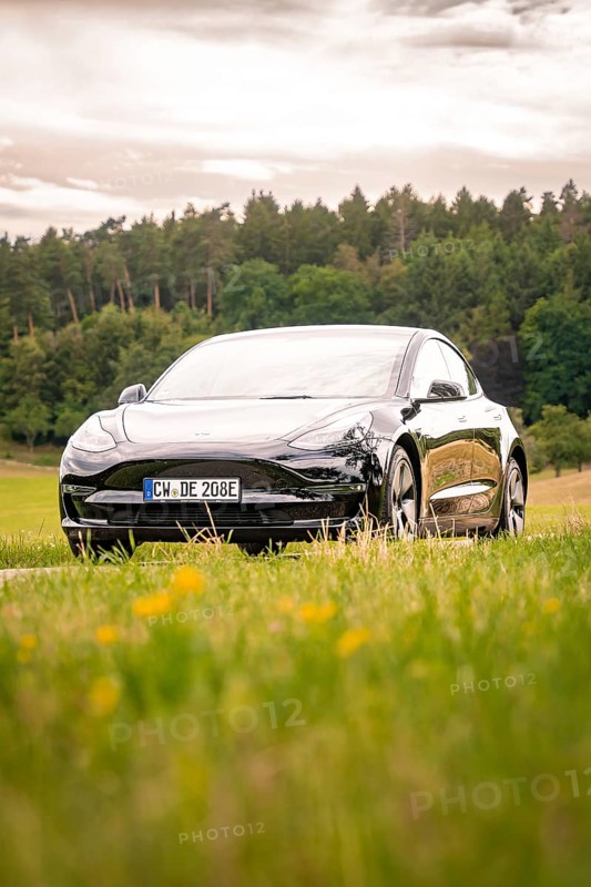 Black car on a country road with a view of green fields and forest, Deer E-Carsharing, Tesla Model 3, Calw, Germany