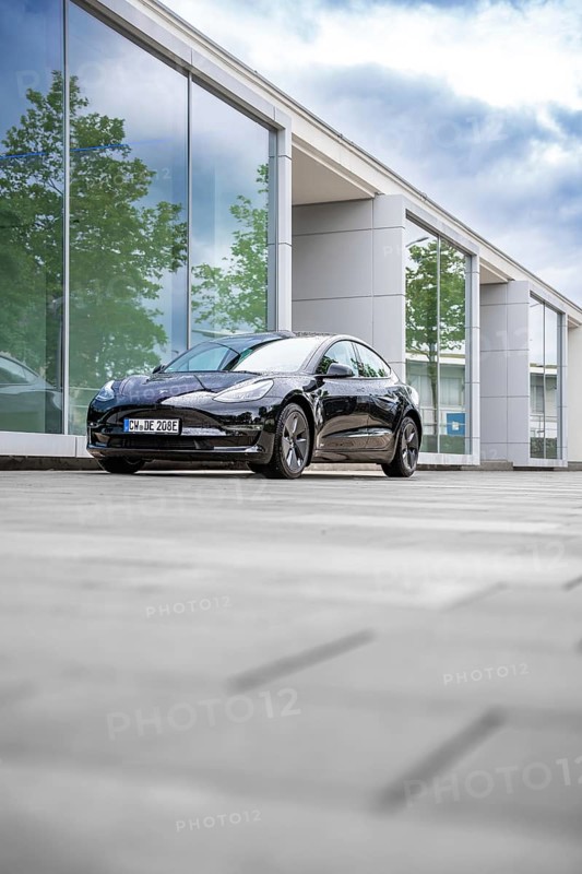 Black Tesla in front of a reflecting glass building on a cloudy day, Deer E-Carsharing, Tesla Model 3, Calw, Germany