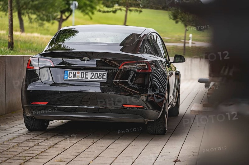 Black car from behind on a road with green landscape in the background, Deer e-Carsharing, Tesla Model 3, Calw, Germany