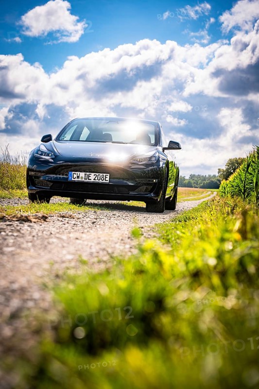Black car driving on a dirt road through picturesque landscape under blue sky, Deer E-Carsharing, Tesla Model 3, Calw, Germany
