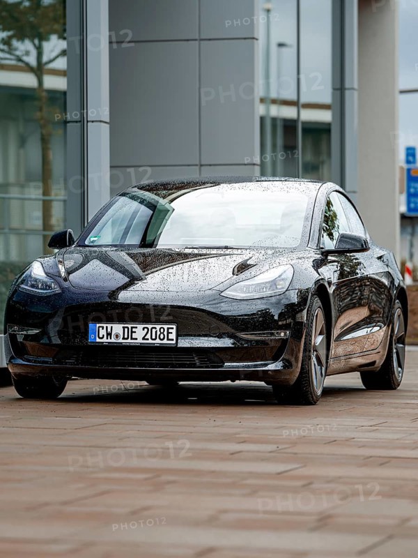 Black car with rain droplets on paint in front of glass buildings, Deer E-Carsharing, Tesla Model 3, Calw, Germany