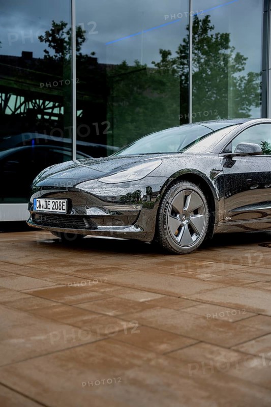 Black car in front of a glass building on rain-wet ground, Deer E-Carsharing, Tesla Model 3, Calw, Germany
