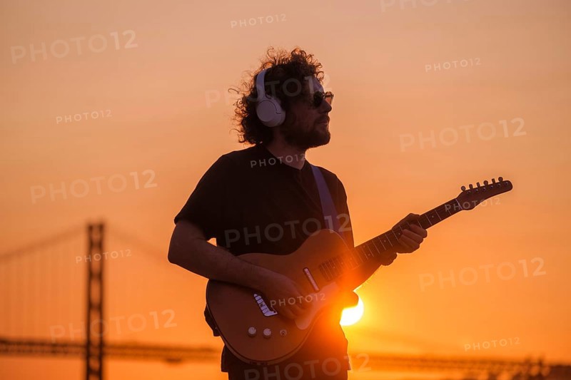 Hipster street musician in black playing electric guitar in street outdoors on sunset