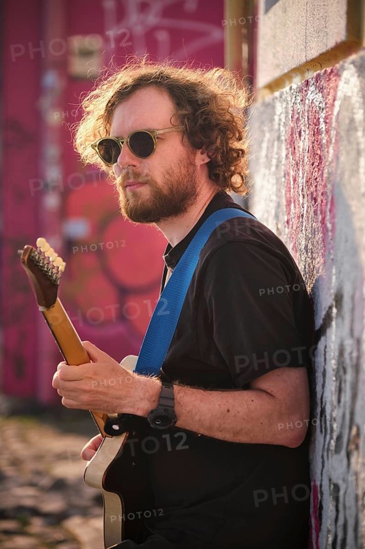 Hipster street musician in black playing electric guitar in the street on sunset leaning on a wall. Lisbon, Portugal
