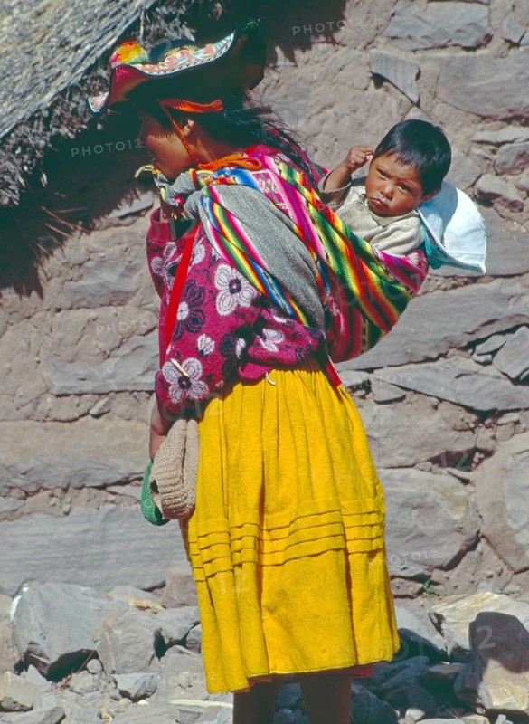 Young woman wearing traditional clothing carries her small child in a traditional way on Isla Taquile in Lake Titicaca, Andean Highlands, Peru, South America, September 1997, vintage, retro, old, historic