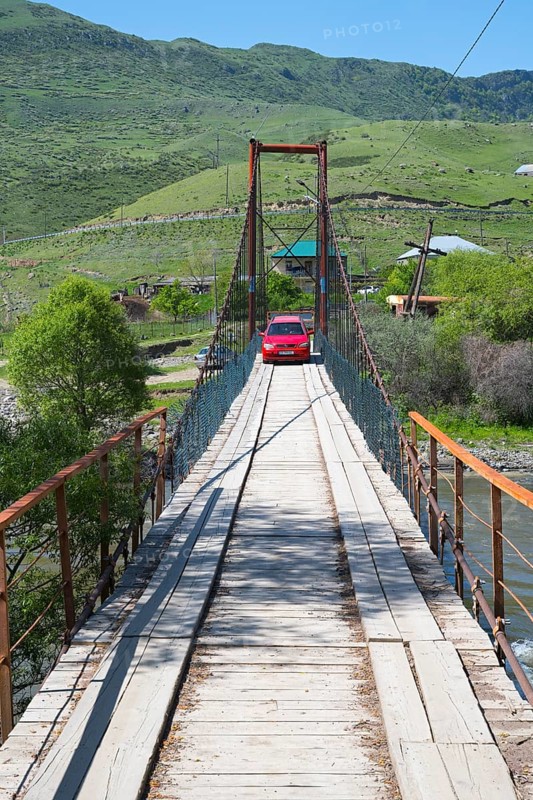 A car drives across a wooden suspension bridge in green surroundings, Kura River near Nijgori, Samtskhe-Javakheti region, Samtskhe-Javakheti, Georgia