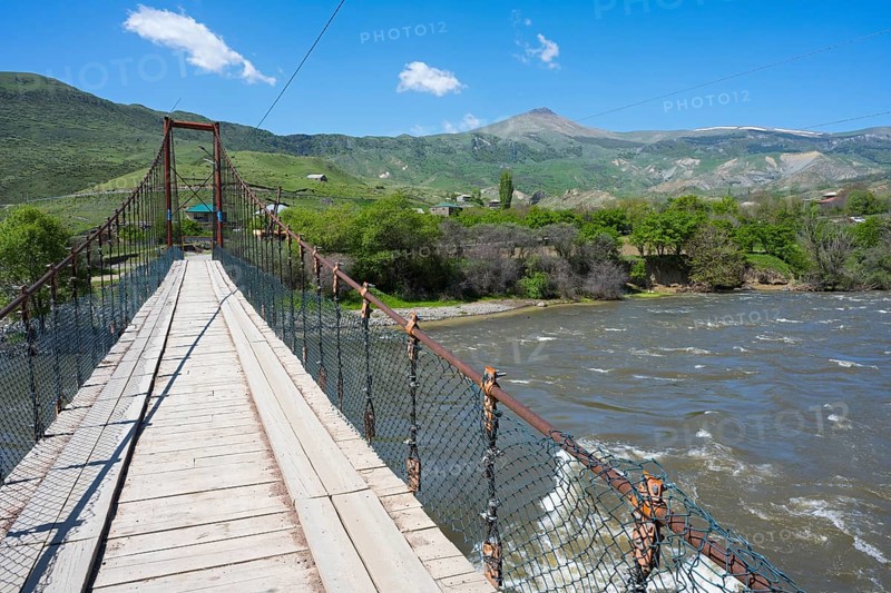 View of a swinging suspension bridge spanning a river, with green hills and a mountain in the background, Kura River near Nijgori, Samtskhe-Javakheti region, Samtskhe-Javakheti, Georgia