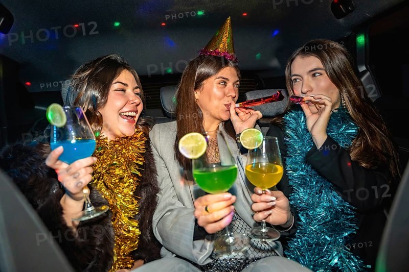 Young women friends celebrating a new year's eve or special occasion, having fun in a car, enjoying colorful cocktails and party blowers, with festive decorations and disco lights