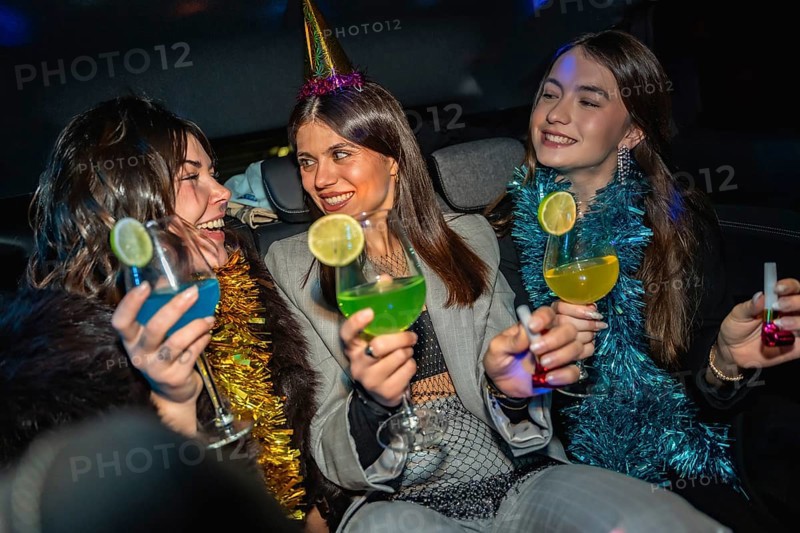 Young women celebrating new year's eve on their way to a party, holding colorful cocktails and wearing festive attire, enjoying a fun road trip at night