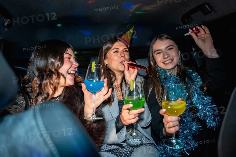 Three happy young women friends celebrating a cheerful new year's eve party in a vehicle, enjoying drinks, party hats, and festive decorations at night