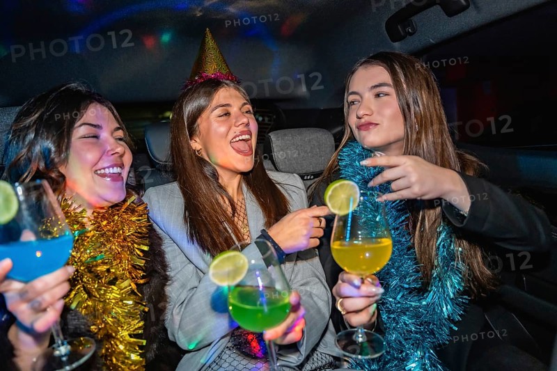 Three young women are happily celebrating a party in a car, enjoying colorful cocktails and good times under vibrant disco lights, creating a festive atmosphere