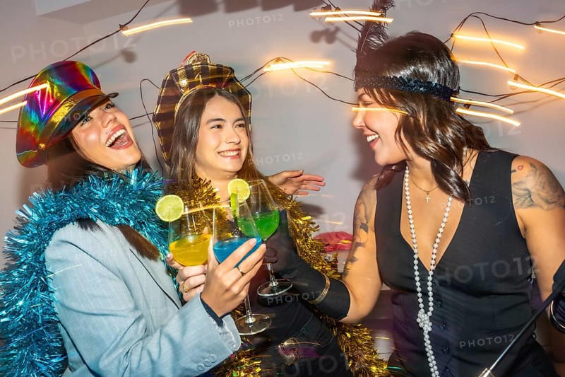 Diverse young adults at a lively new years eve costume party, dressed in festive outfits and headwear, laughing and toasting colorful cocktails in close up celebration