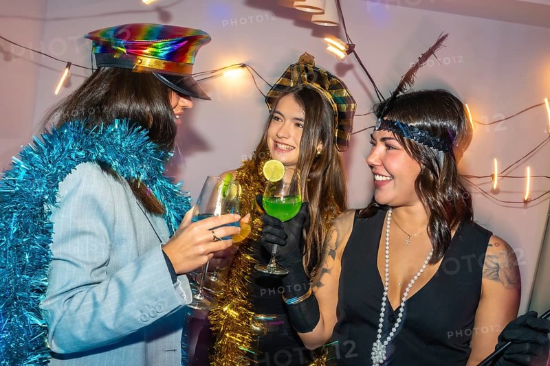 Three happy young women enjoying a festive new year's eve or costume party with drinks and tinsel decorations, sharing smiles and creating joyful celebration moments together