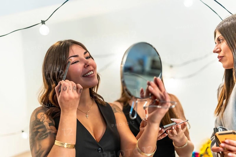 Young diverse women enjoying a fun time together, preparing for a special occasion party at home by applying cosmetics and chatting, focusing on beauty and friendship