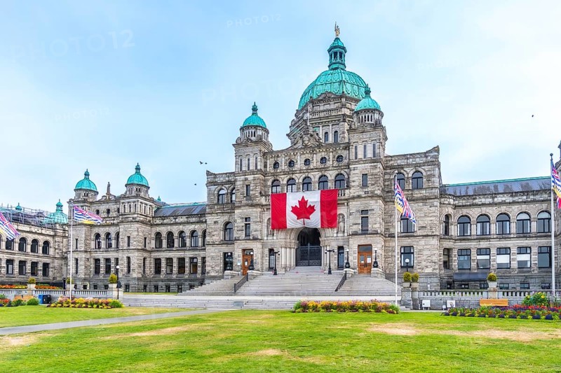 British columbia parliament buildings with large canadian flag hanging from the front during a sunny summer day in victoria, british columbia