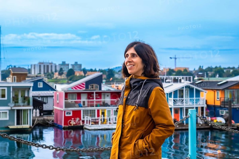 Happy tourist admiring the colorful floating houses of fisherman's wharf park in victoria, british columbia, with the city skyline in the background on a beautiful summer day