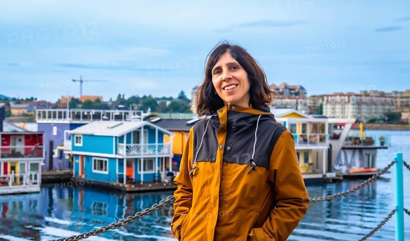 Happy tourist smiling brightly with vibrant floating houses lining the harbor in the background on a sunny summer day in victoria, british columbia, canada