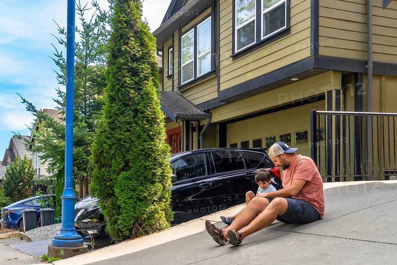 Father and son enjoying quality time together, sitting on their driveway on a sunny summer day, fostering a strong family bond in a peaceful suburban setting