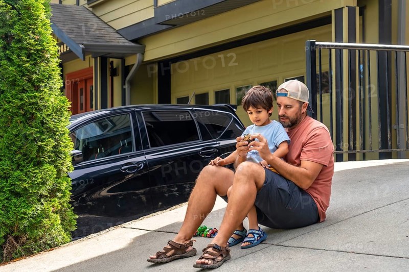 Father and son bonding while playing with a toy car on the driveway, sharing joyful moments together outside their home on a bright, sunny day filled with laughter and love