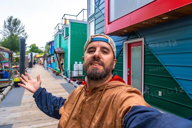 Tourist taking a selfie and showing colorful floating homes in fisherman's wharf park, a popular tourist destination in victoria, british columbia, canada