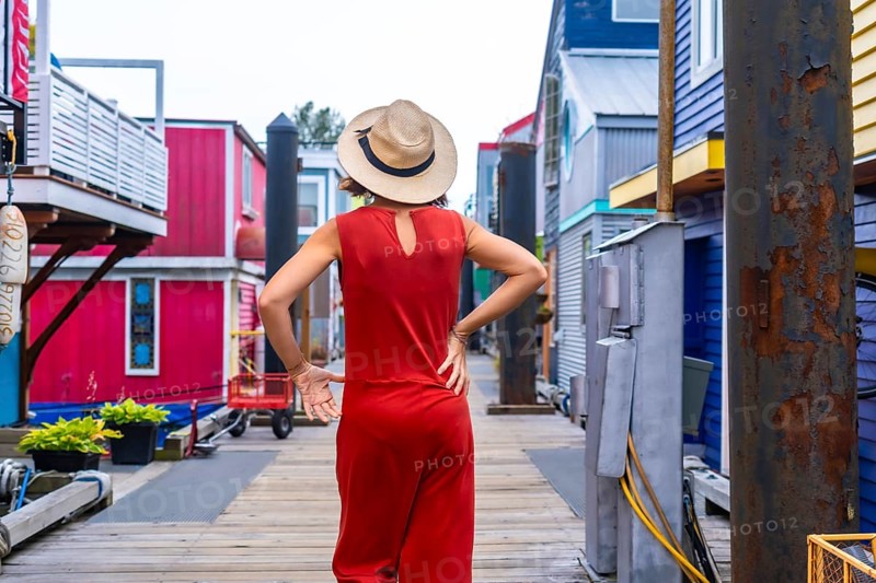 Tourist wearing a red jumpsuit and straw hat walking at fisherman's wharf park, a colorful floating house community, in victoria, british columbia, canada