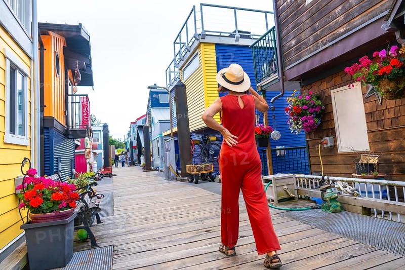 Tourist wearing a straw hat and a red jumpsuit walking in fisherman's wharf park, a colorful floating house community in victoria, british columbia, canada, during a sunny summer day