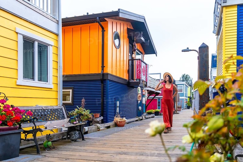 Tourist walking on a wooden walkway. Wearing a straw hat and a red jumpsuit. Exploring the colorful floating houses of fisherman's wharf park in victoria. British columbia. During a sunny summer day