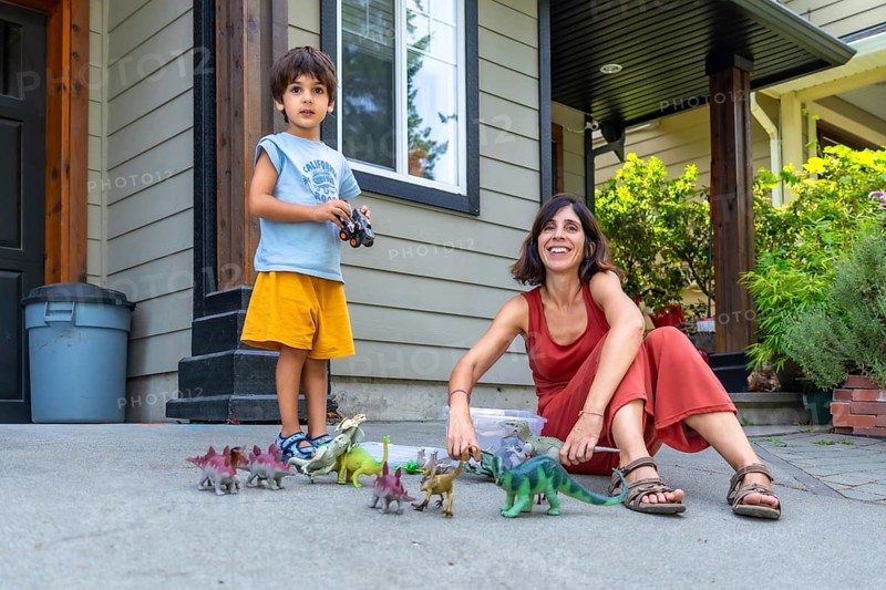 Happy mother and son enjoying quality time together, playing with dinosaur toys on their porch in canada during a sunny summer day, creating a heartwarming scene of family bonding