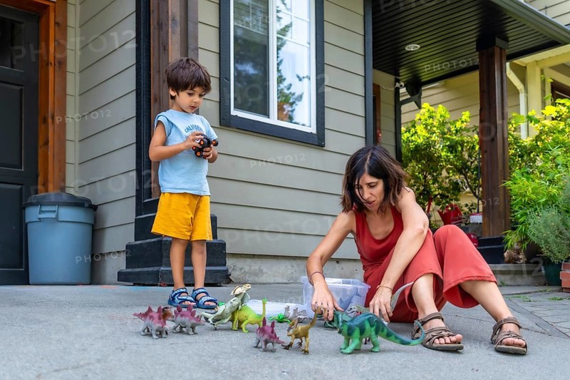 Mother and son enjoying quality time together, playing with dinosaur toys on the porch of their house, fostering imagination and creating joyful memories