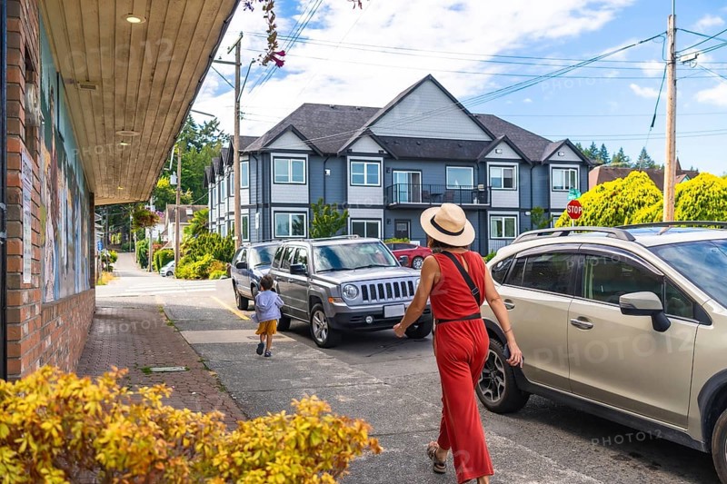 Tourists are walking along a street with parked cars in chemainus, a town known for its outdoor murals, located on vancouver island, british columbia, canada