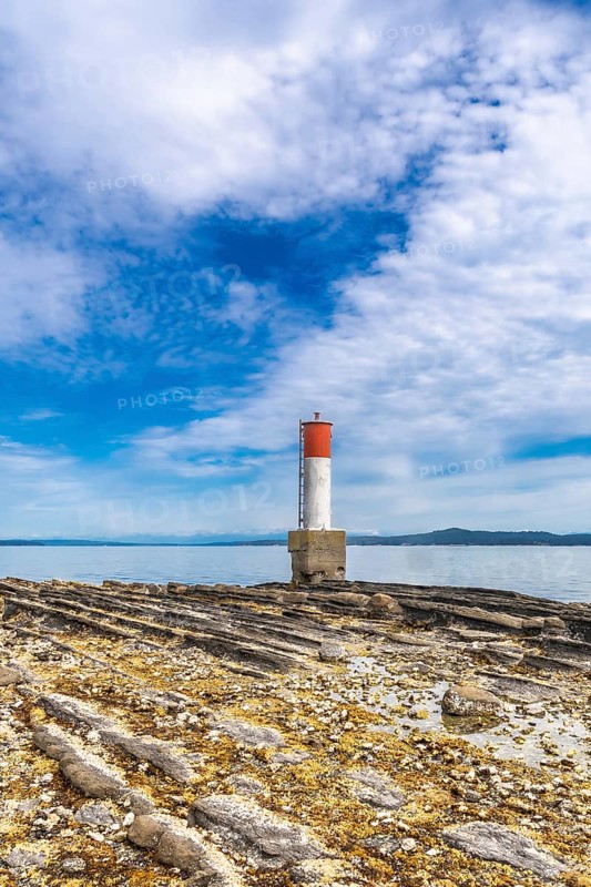 Red and white lighthouse standing on a rocky beach with a blue sky and clouds in the background in chemainus, vancouver island, british columbia, canada