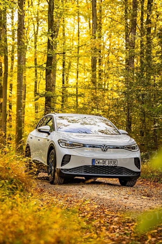 An SUV drives on a forest path in autumn surrounded by yellow leaves under bright sunlight, VW ID4 electric car, deer car sharing, Calw, Germany