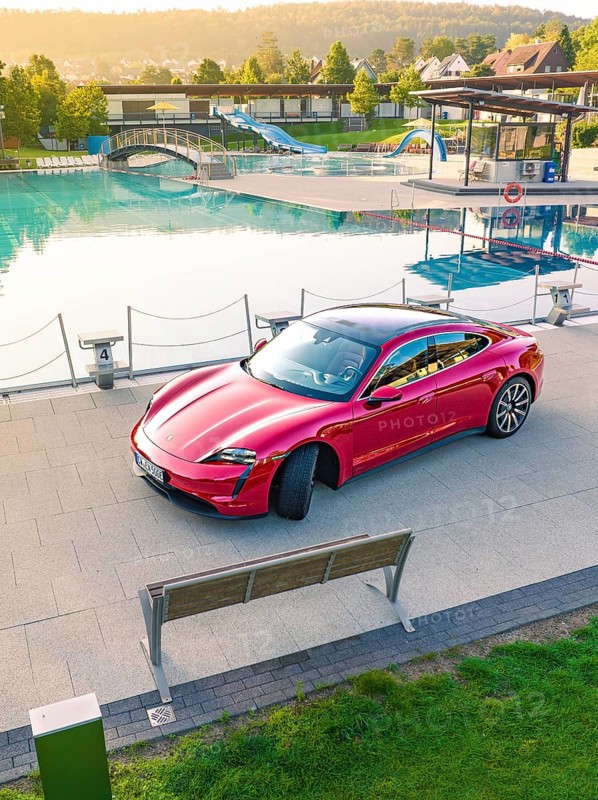 Red sports car parked next to a swimming pool and park bench in daylight, Porsche Taycan, Deer Carsharing, Calw, Germany