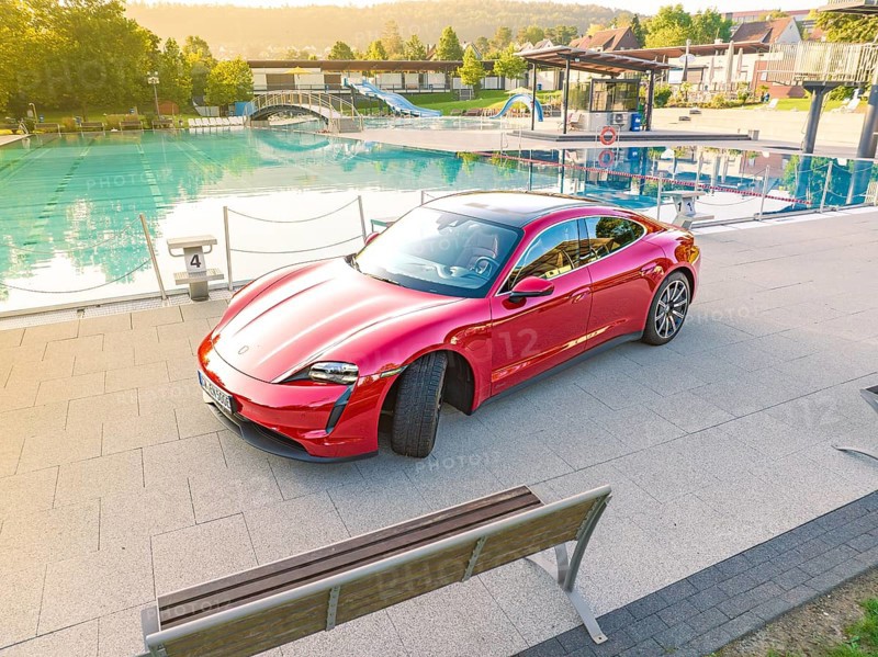 Red sports car next to a swimming pool and park bench in daylight, Porsche Taycan, Deer Carsharing, Calw, Germany