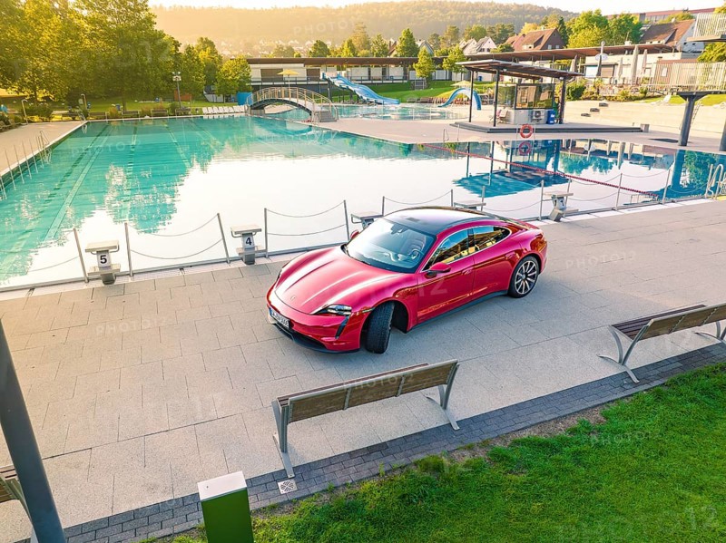 Red Porsche Taycan in parking lot next to swimming pool in relaxed landscape, Porsche Taycan, Deer Carsharing, Calw, Germany