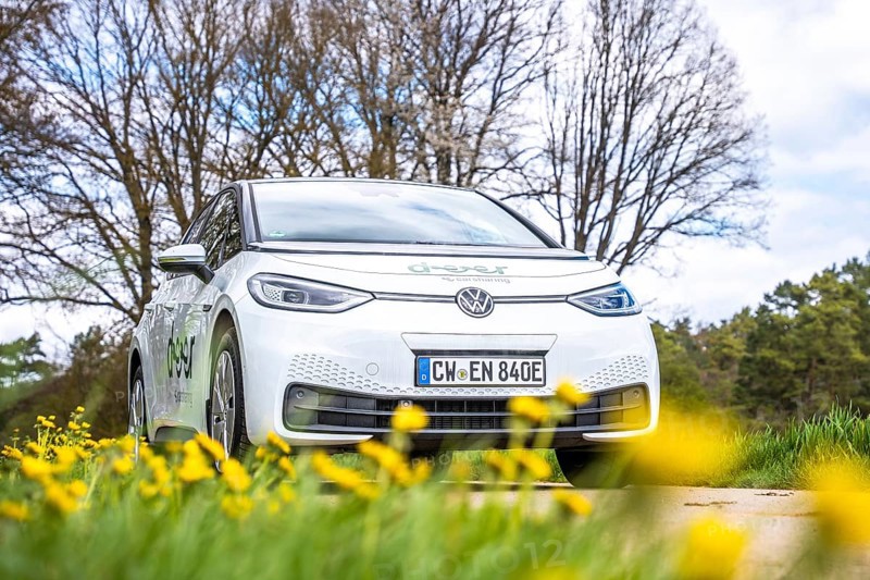 A white car is parked in a meadow with yellow flowers and bare trees, ID3 VW, deer car sharing. Calw, Germany