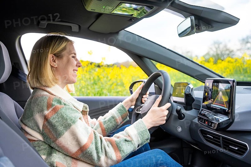 A smiling woman sits in a car and drives through a blooming landscape, ID3 VW, deer car sharing. Calw, Germany