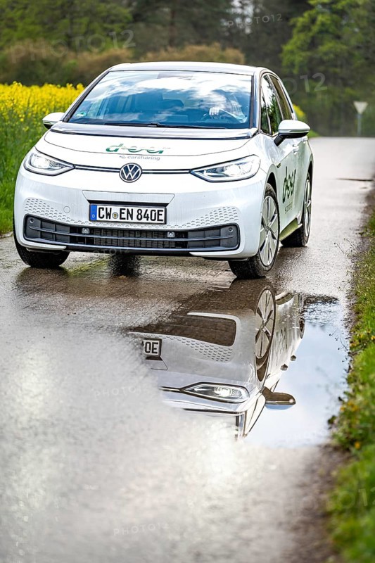 Car on wet road with clear reflection in the puddle, surrounded by green nature, ID3 VW, deer car sharing. Calw, Germany