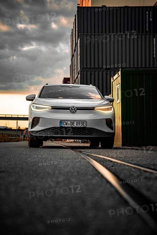 White car drives past container warehouse at sunset, dramatic urban scene, VW ID4 electric car, deer car sharing, Calw, Germany