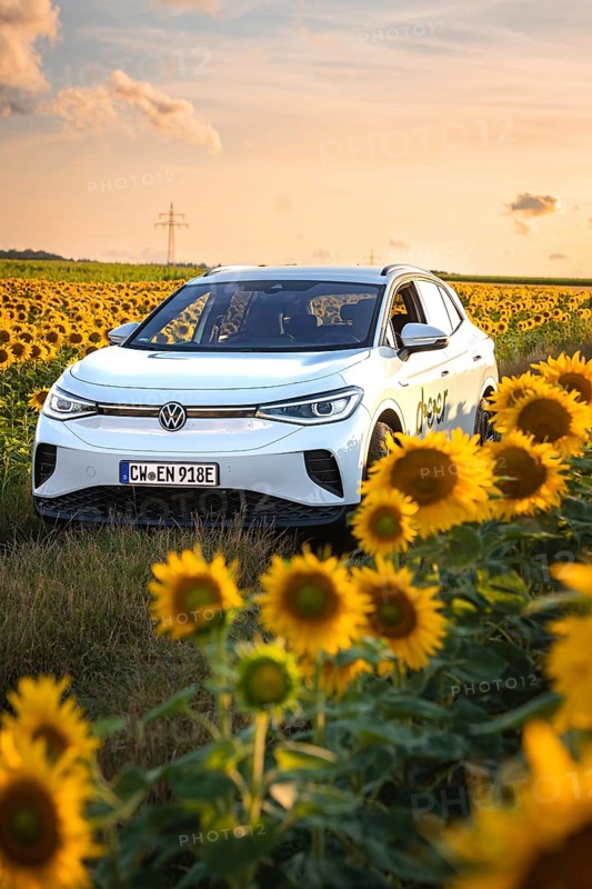 A white car drives through a blooming sunflower field in sunny sky, VW ID4 electric car, deer car sharing, Calw, Germany